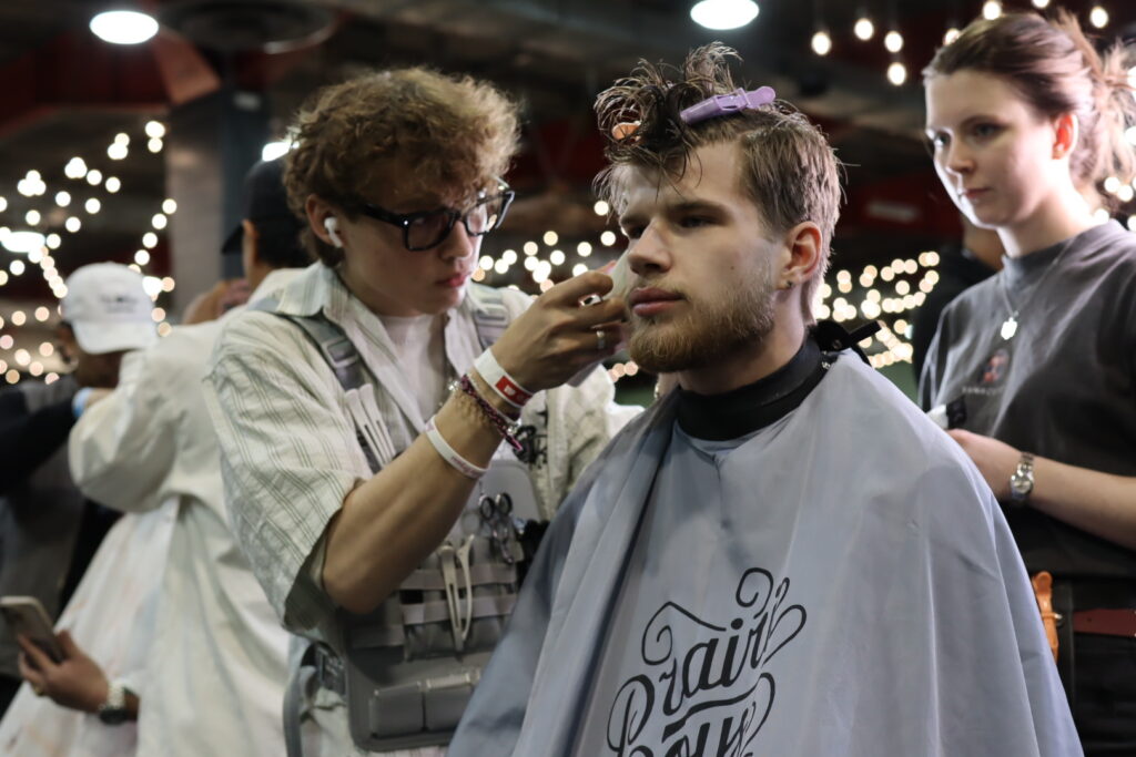 Barber with curly hair is cutting the hair of another man sitting in a chair